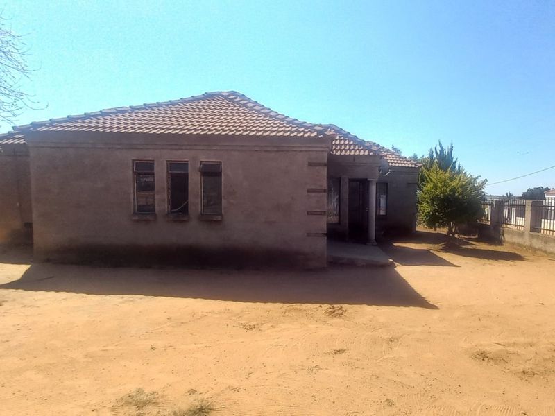Front view of a single-story house with a tiled roof, featuring an unpaved yard and perimeter boundary walling.