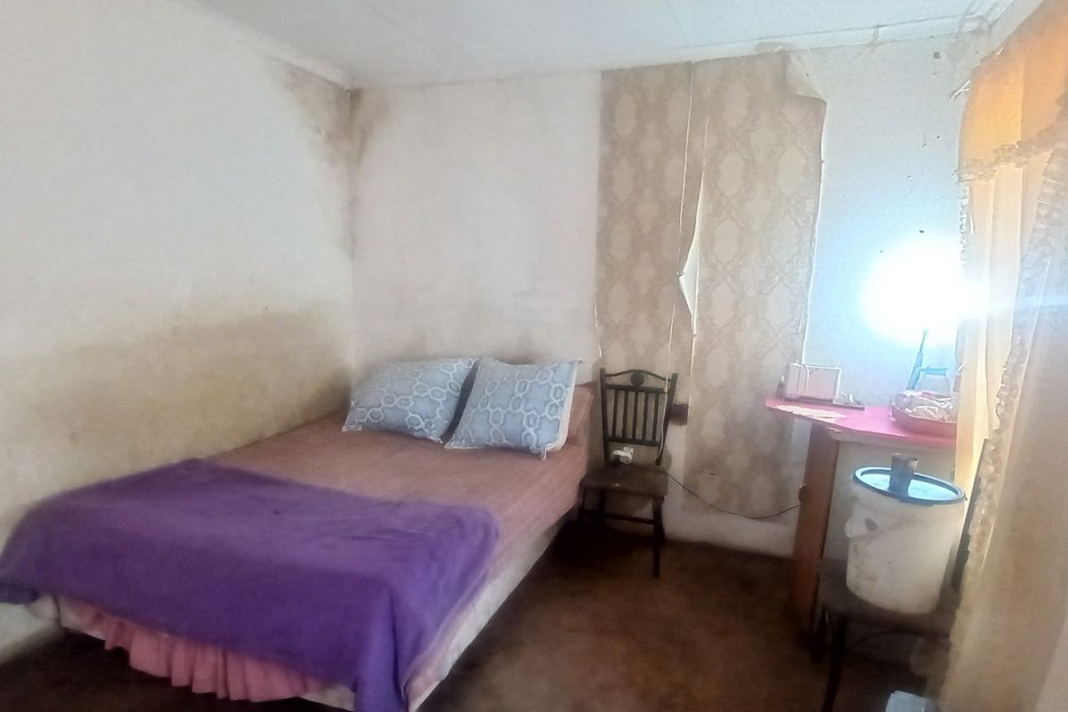 A bedroom interior showing significant wall staining and peeling wallpaper, indicating a need for cosmetic renovation and surface repairs.