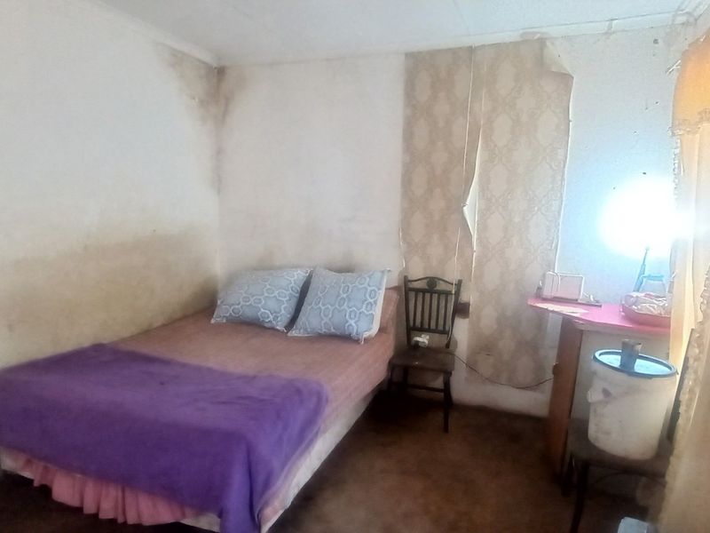 A bedroom interior showing significant wall staining and peeling wallpaper, indicating a need for cosmetic renovation and surface repairs.