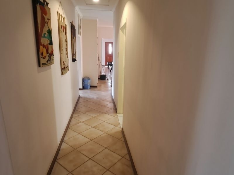 A long, neutral-toned hallway featuring diamond-patterned floor tiles and recessed ceiling lighting, providing access to various rooms within the home.