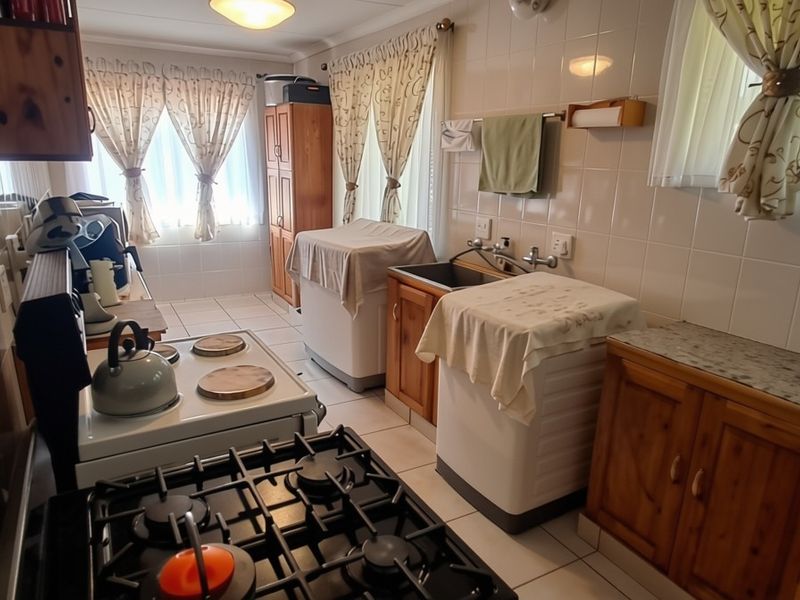 A functional kitchen featuring tiled walls, wooden cabinetry, a gas hob, and a stainless steel sink, offering a practical layout for daily use.