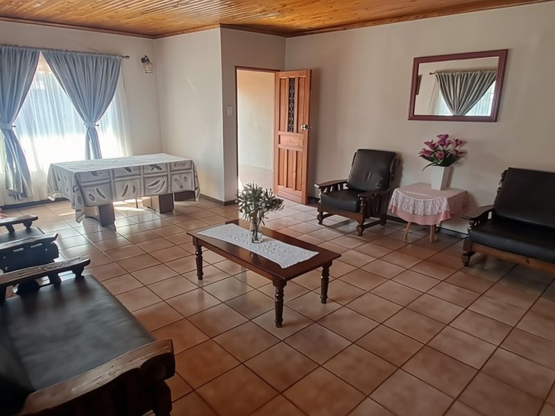 Spacious living room featuring tiled flooring and a timber-paneled ceiling, offering a traditional layout with direct access to adjacent rooms.
