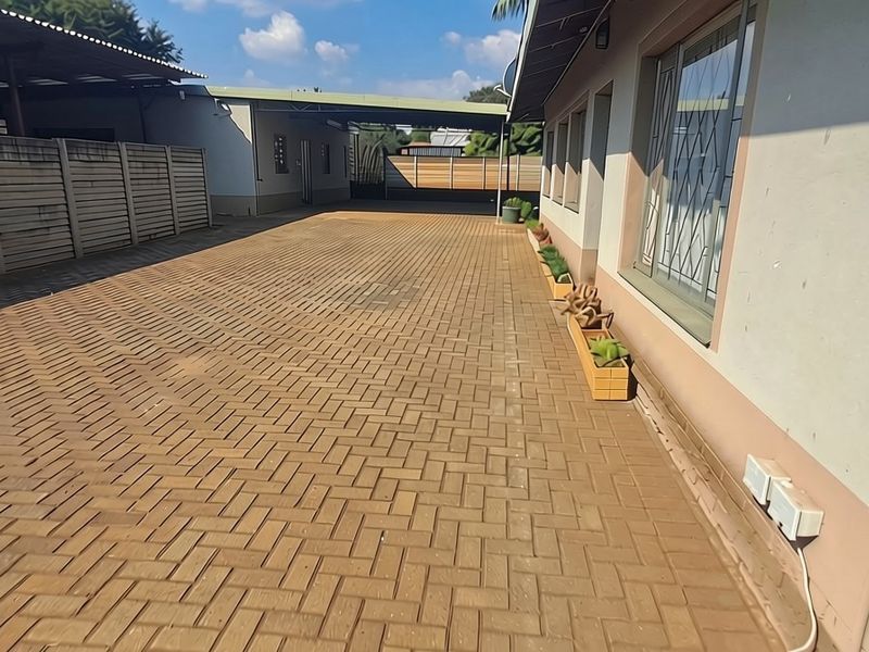 A paved driveway leading to a carport, featuring a precast concrete boundary wall and exterior wall finishes.