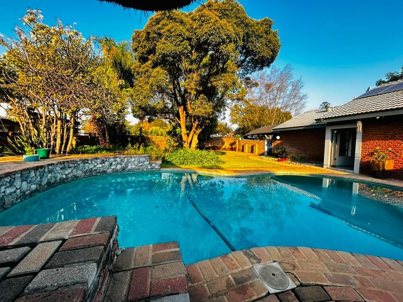 A well-maintained outdoor pool area featuring a stone retaining wall, brick paving, and a landscaped garden with mature trees.