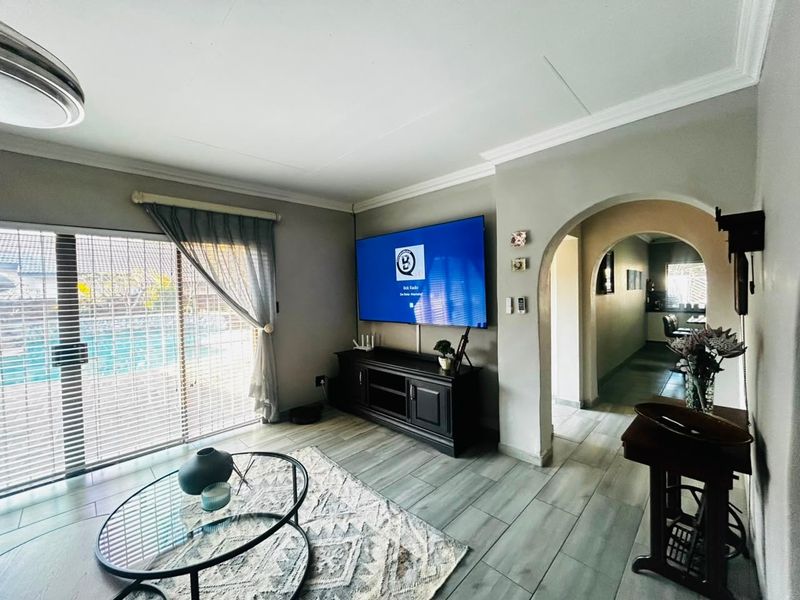A well-maintained living room featuring tiled flooring, a coved ceiling, and a large sliding glass door providing access to the outdoor pool area.