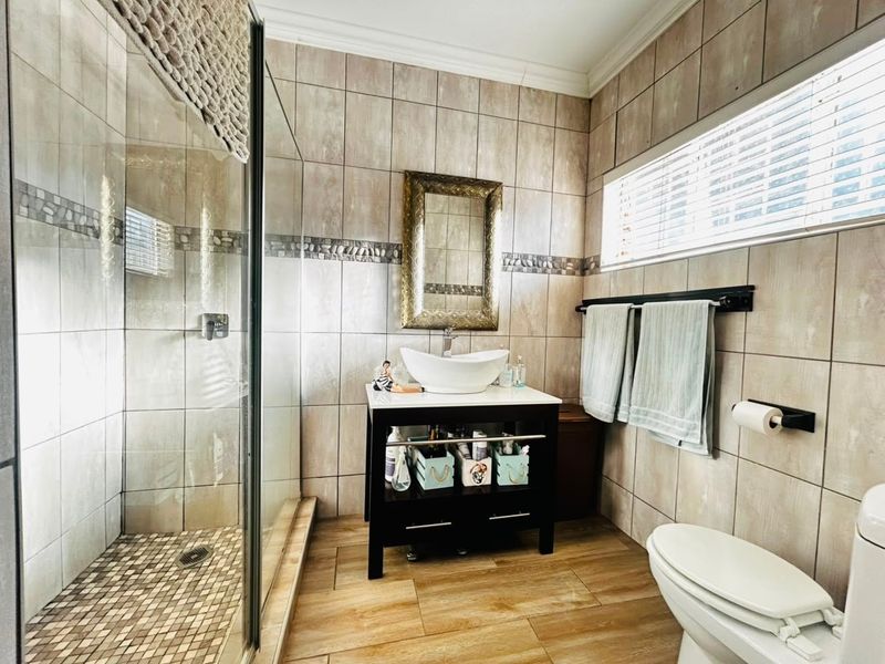 A well-maintained bathroom featuring a glass-enclosed shower, a modern vessel sink vanity, and neutral wall and floor tiling.