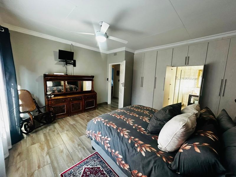 Spacious bedroom featuring built-in cupboards, tiled flooring, a ceiling fan, and direct access to an en-suite bathroom.