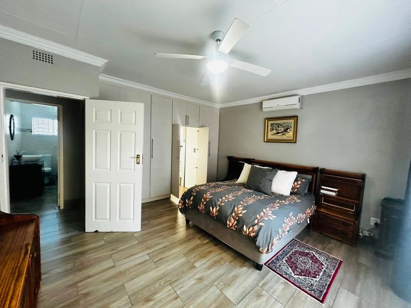 Spacious bedroom featuring built-in cupboards, tiled flooring, ceiling fan, air conditioning, and direct access to an en-suite bathroom.