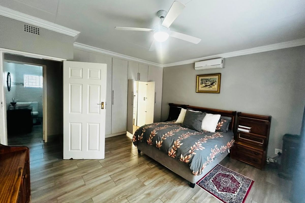 Spacious bedroom featuring built-in cupboards, tiled flooring, ceiling fan, air conditioning, and direct access to an en-suite bathroom.