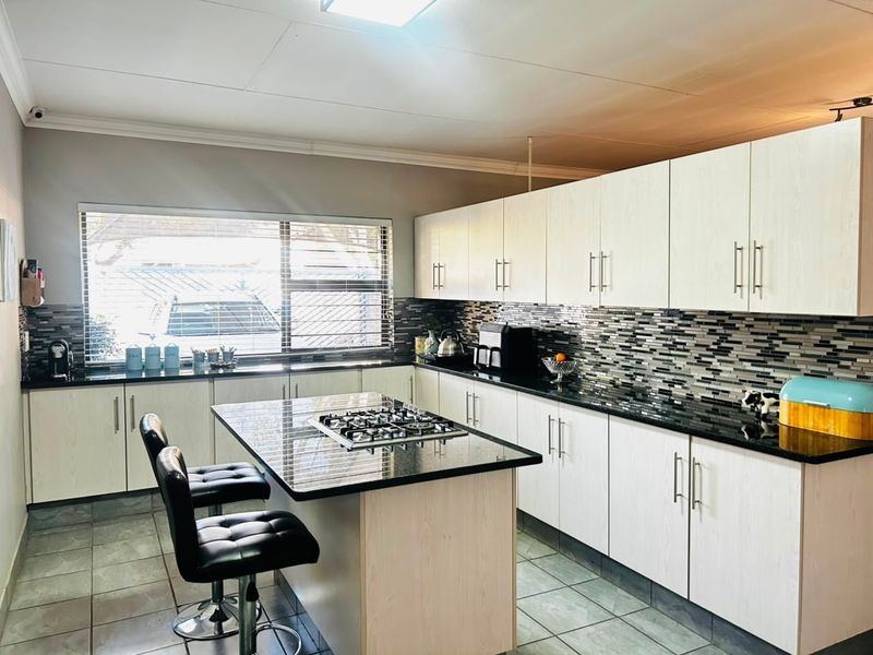 Modern kitchen featuring light wood-grain cabinetry, black granite countertops, a central island with a built-in gas hob, and a decorative mosaic tile backsplash.