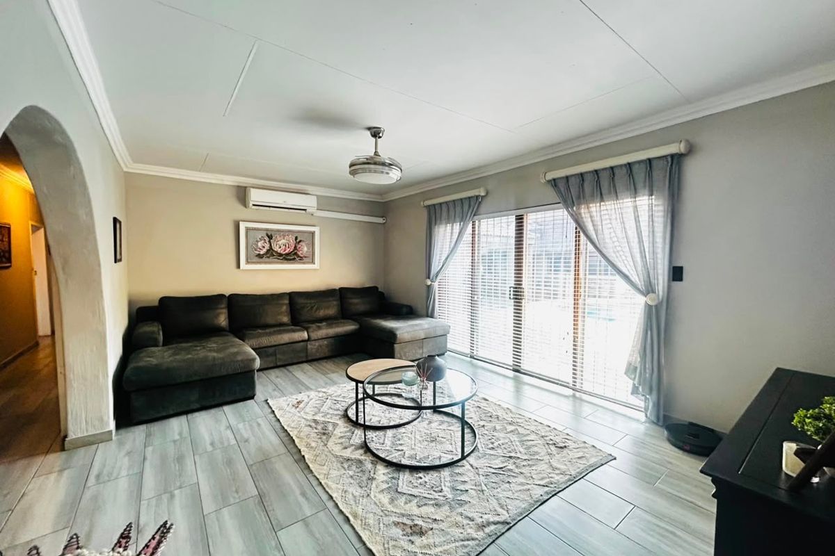 A well-lit living room featuring tiled flooring, a ceiling fan, split-system air conditioning, and large sliding glass doors providing access to the exterior.