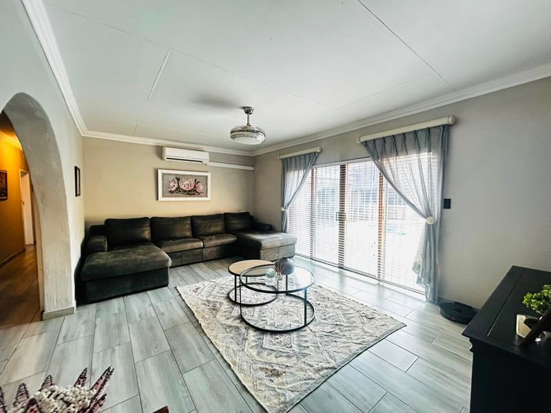 A well-lit living room featuring tiled flooring, a ceiling fan, split-system air conditioning, and large sliding glass doors providing access to the exterior.