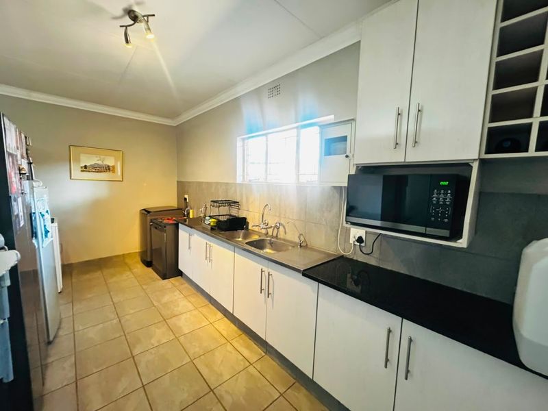 A functional kitchen featuring white cabinetry, black granite countertops, stainless steel sink, tiled backsplash, and tiled flooring.