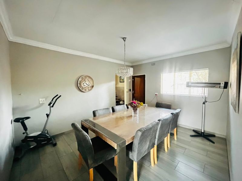 A well-lit dining room featuring modern tiled flooring, neutral wall tones, and a decorative pendant light fixture.