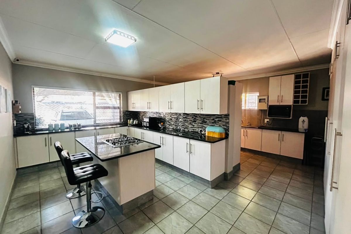 Spacious kitchen featuring white cabinetry, granite countertops, a central island with a gas hob, and tiled flooring with a mosaic backsplash.