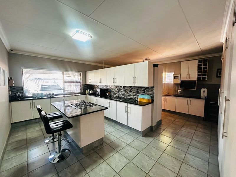 Spacious kitchen featuring white cabinetry, granite countertops, a central island with a gas hob, and tiled flooring with a mosaic backsplash.