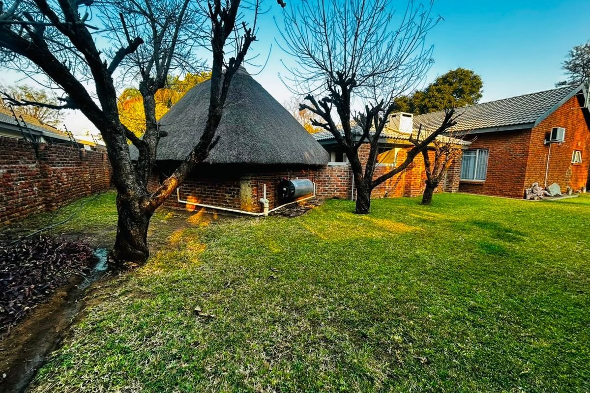 Rear garden view featuring a traditional thatched roof structure, brick exterior walls, and a well-maintained lawn area.
