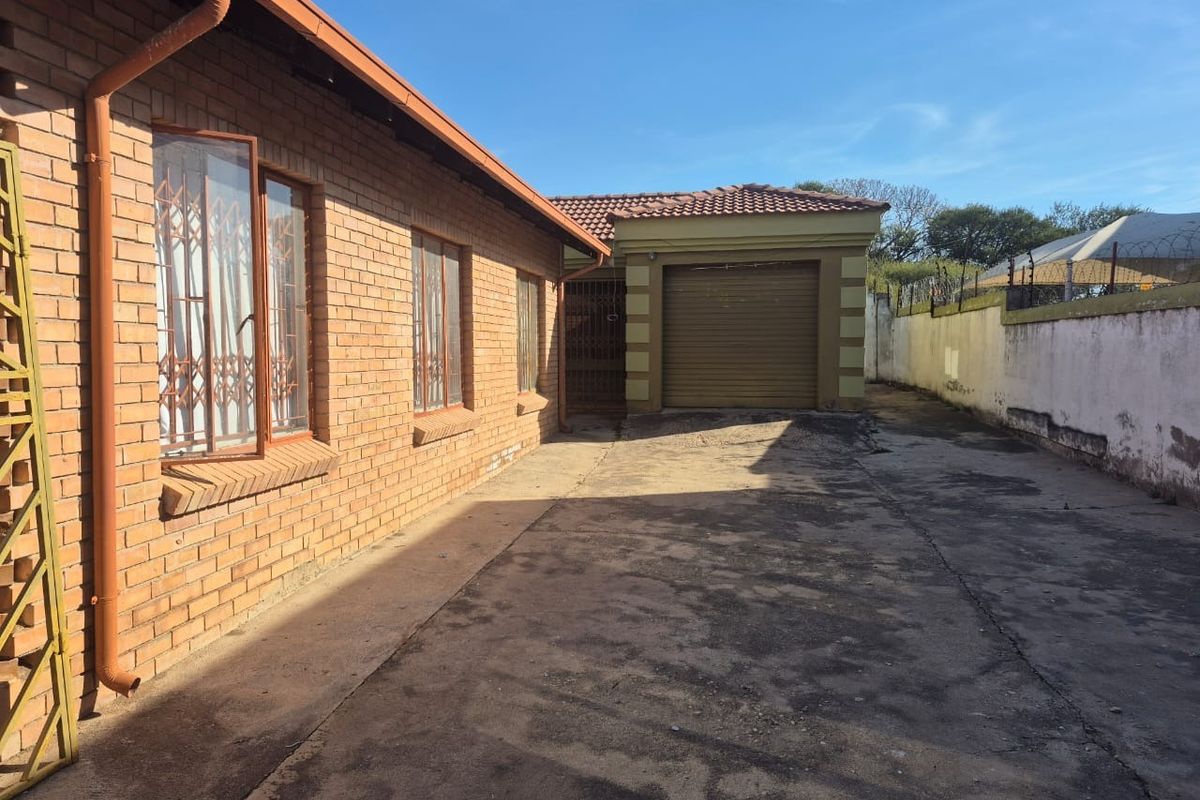 Rear exterior view showing a face brick house, concrete driveway, and a single garage with a perimeter wall.