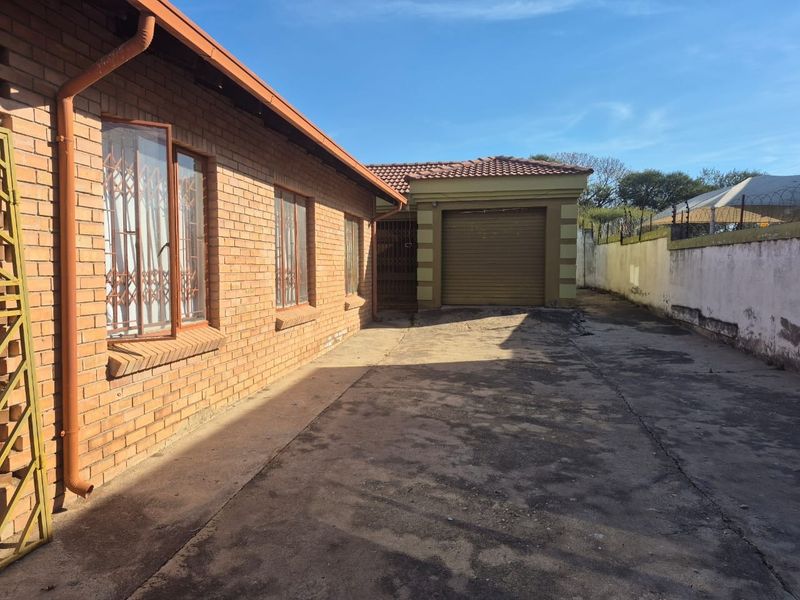 Rear exterior view showing a face brick house, concrete driveway, and a single garage with a perimeter wall.