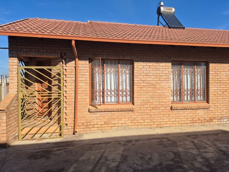 A well-maintained face brick house exterior featuring a tiled roof, solar water heating system, and secure metal gates over the windows and entrance.
