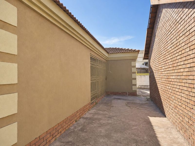 A side exterior walkway featuring concrete paving, a security gate, and a combination of plastered and brick wall finishes.