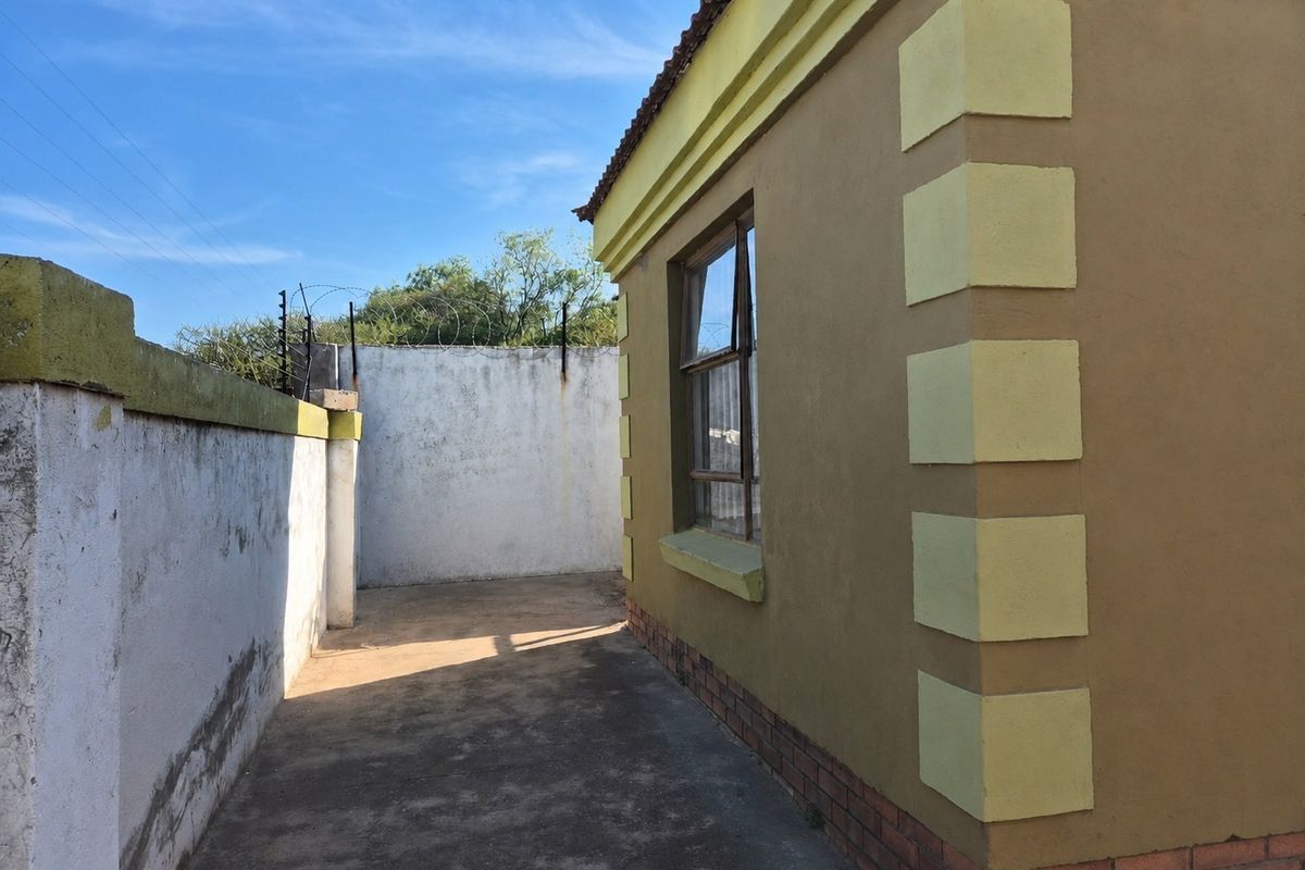 A view of the rear exterior area featuring a paved walkway, perimeter wall with electric fencing, and the side facade of the house.