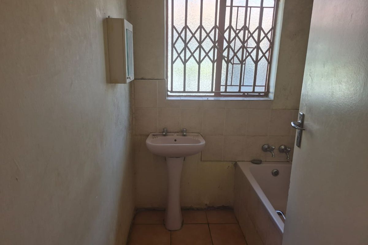 A dated bathroom featuring a pedestal basin, bathtub, and security-fitted window, requiring cosmetic updates and modernization of finishes.