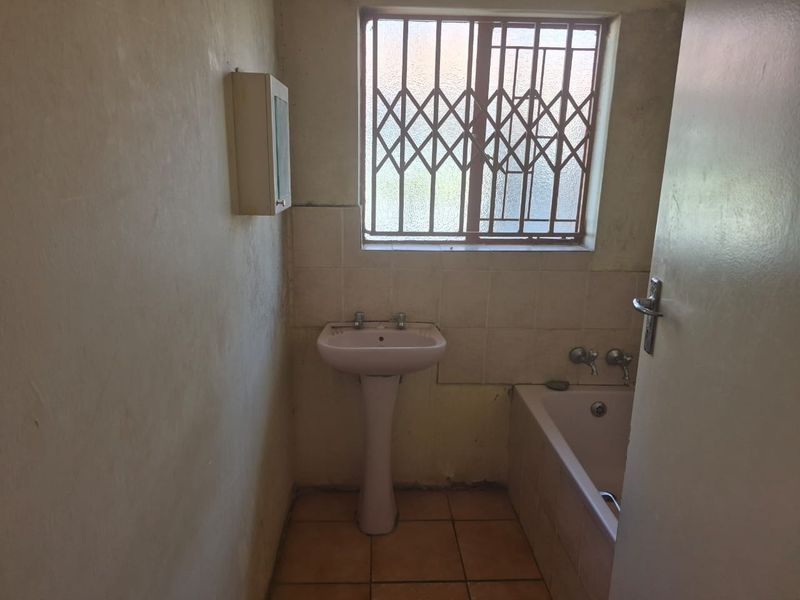 A dated bathroom featuring a pedestal basin, bathtub, and security-fitted window, requiring cosmetic updates and modernization of finishes.