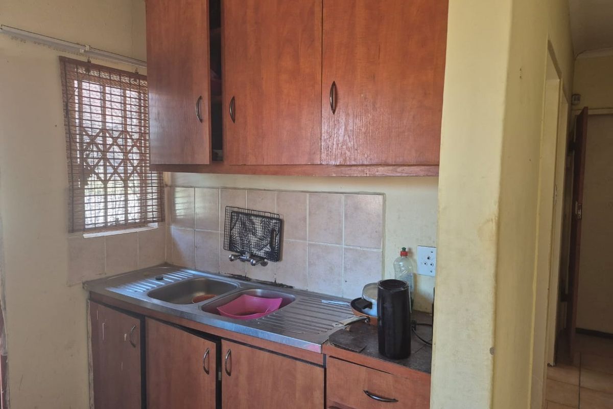 A compact kitchen featuring wooden cabinetry, a stainless steel double sink, and tiled backsplash, offering a functional space ready for modernization.