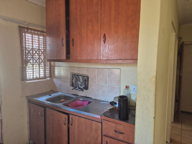 A compact kitchen featuring wooden cabinetry, a stainless steel double sink, and tiled backsplash, offering a functional space ready for modernization.