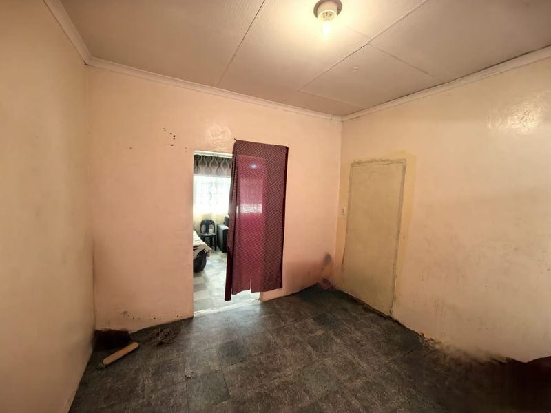 An empty bedroom featuring tiled flooring and basic finishes, requiring cosmetic updates and wall repairs to improve its overall condition.