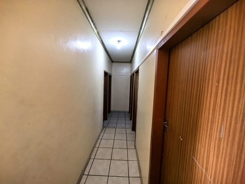A narrow interior hallway featuring tiled flooring and multiple wooden door frames, providing access to various rooms within the property.