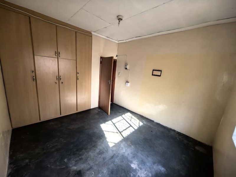 An empty bedroom featuring built-in wooden cupboards, dark flooring, and visible electrical wiring, requiring cosmetic updates and repairs.