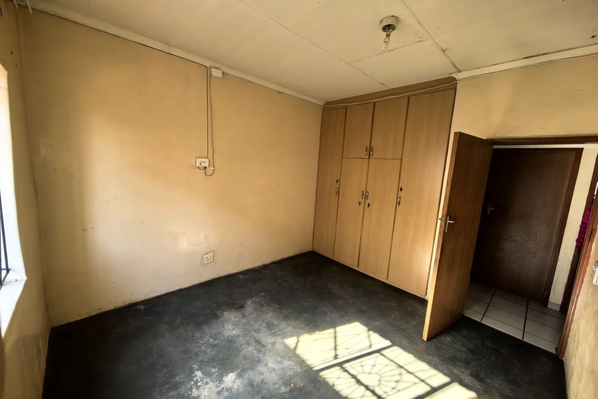 An empty bedroom featuring built-in wooden cupboards, tiled flooring, and neutral wall finishes, offering a blank canvas for renovation or interior design updates.