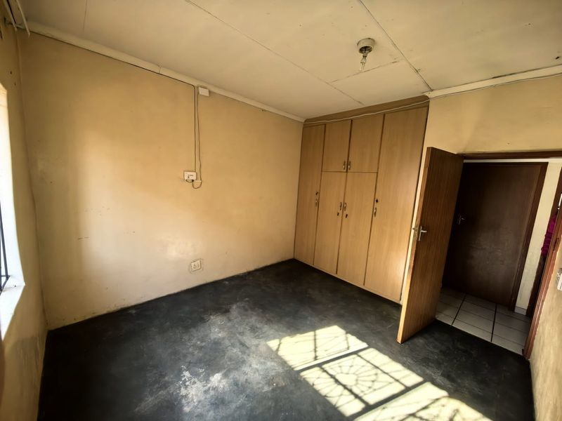 An empty bedroom featuring built-in wooden cupboards, tiled flooring, and neutral wall finishes, offering a blank canvas for renovation or interior design updates.