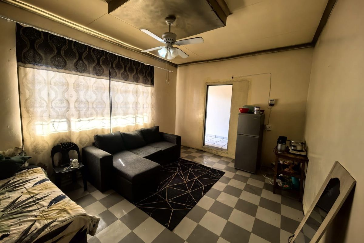 A living area featuring tiled flooring and a ceiling fan, showing signs of wear on the walls and ceiling that would benefit from renovation.