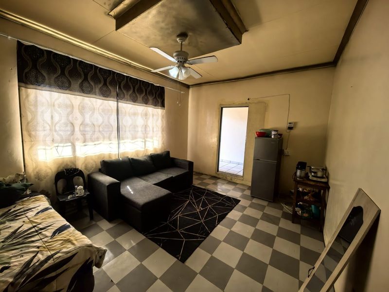 A living area featuring tiled flooring and a ceiling fan, showing signs of wear on the walls and ceiling that would benefit from renovation.