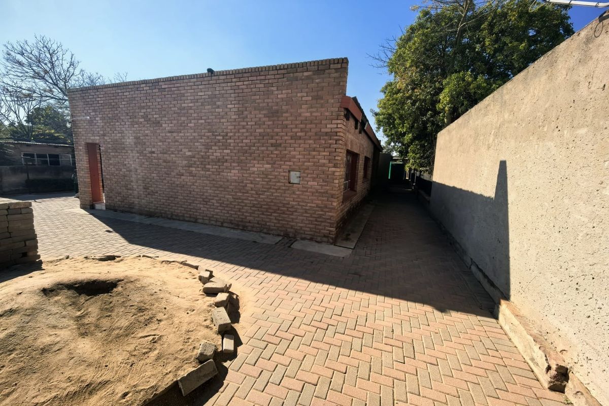 A view of the rear exterior featuring a face brick building facade, paved pathways, and a boundary wall.