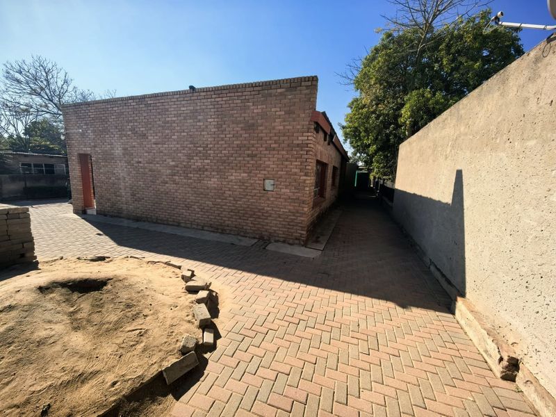 A view of the rear exterior featuring a face brick building facade, paved pathways, and a boundary wall.