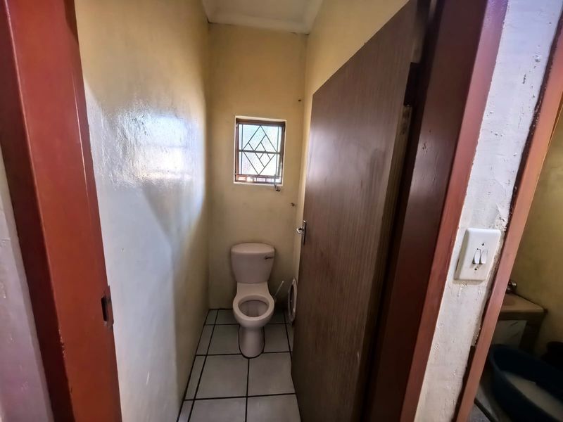 A compact, functional bathroom featuring a standard toilet, tiled flooring, and a small window with security bars.