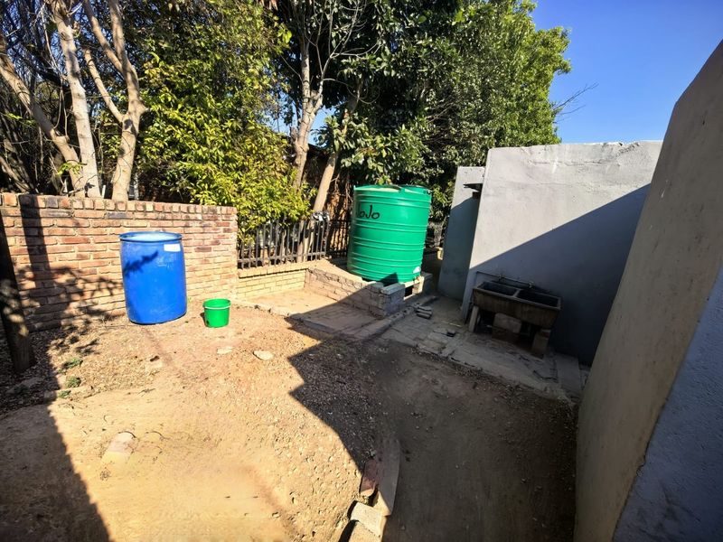Rear outdoor utility area featuring a brick boundary wall, a water storage tank, and a concrete wash trough.