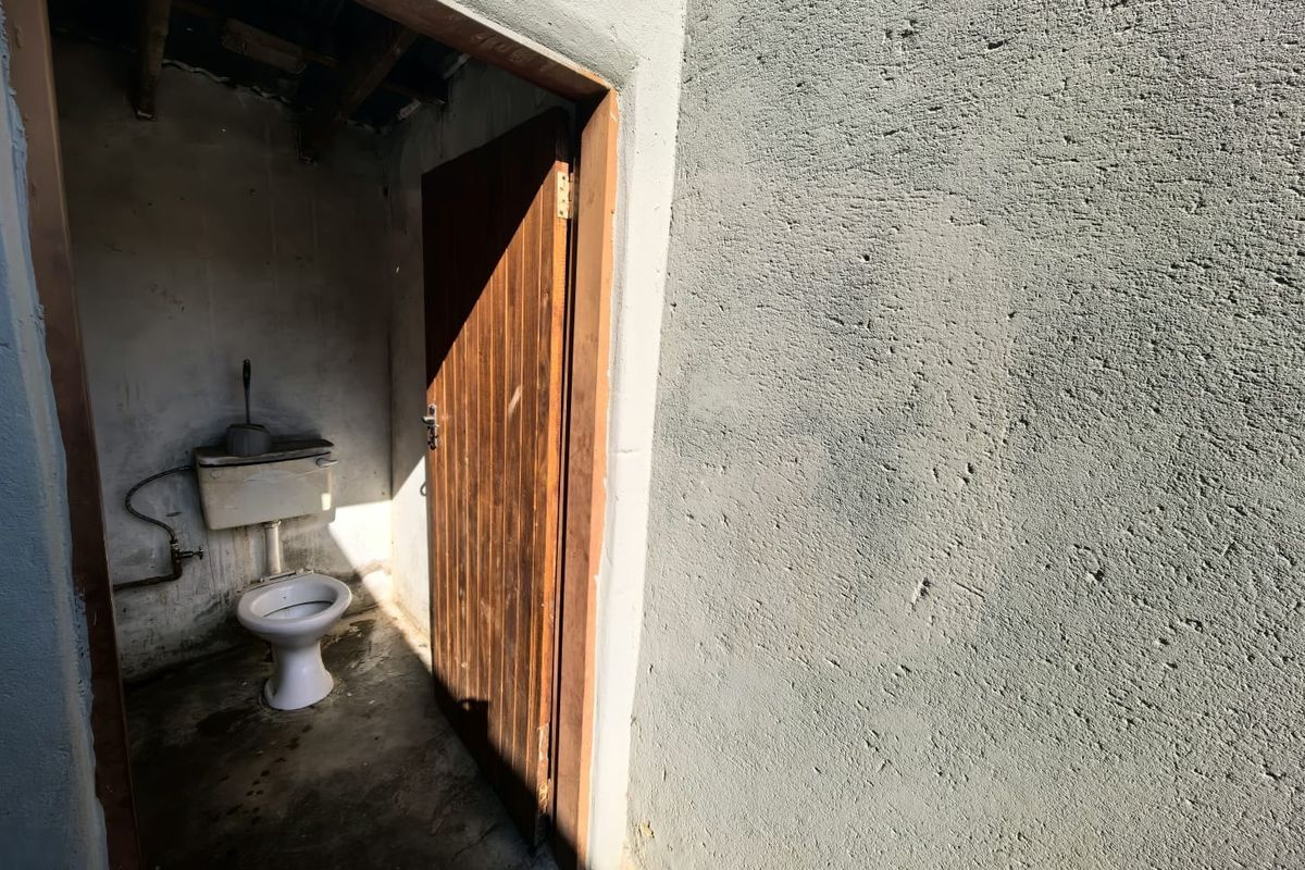A basic, unfinished outdoor or utility bathroom featuring a standard toilet and exposed concrete walls and flooring.
