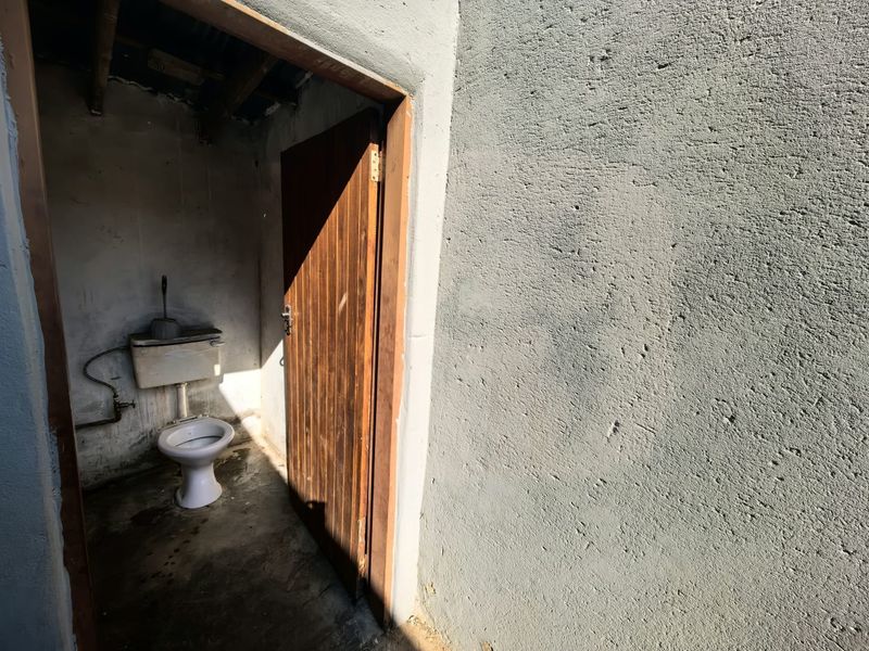 A basic, unfinished outdoor or utility bathroom featuring a standard toilet and exposed concrete walls and flooring.
