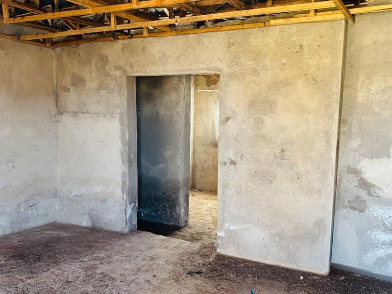 An interior space in shell condition featuring exposed timber roof trusses and unfinished masonry walls, requiring significant renovation and finishing work.