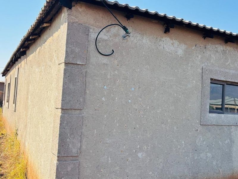Exterior view of the property showing the rear wall, tiled roof, and aluminium window frames with visible weathered plaster and exposed wiring.