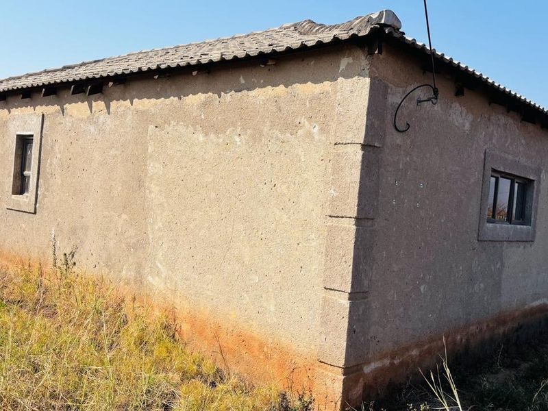 Exterior view of a detached dwelling showing weathered plaster walls, tiled roofing, and aluminium window frames in need of maintenance.