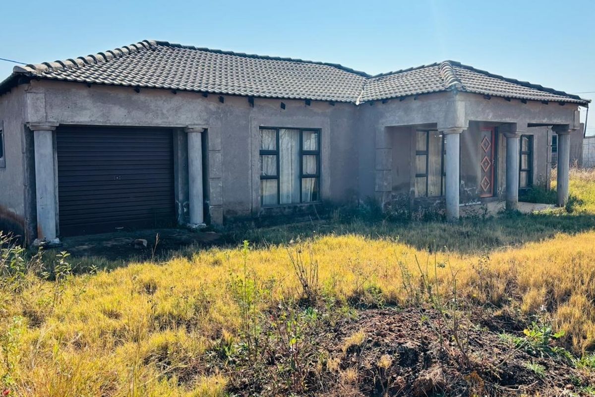 Front elevation of a single-story house featuring a tiled roof, integrated garage, and concrete columns, set on a large plot with overgrown landscaping.