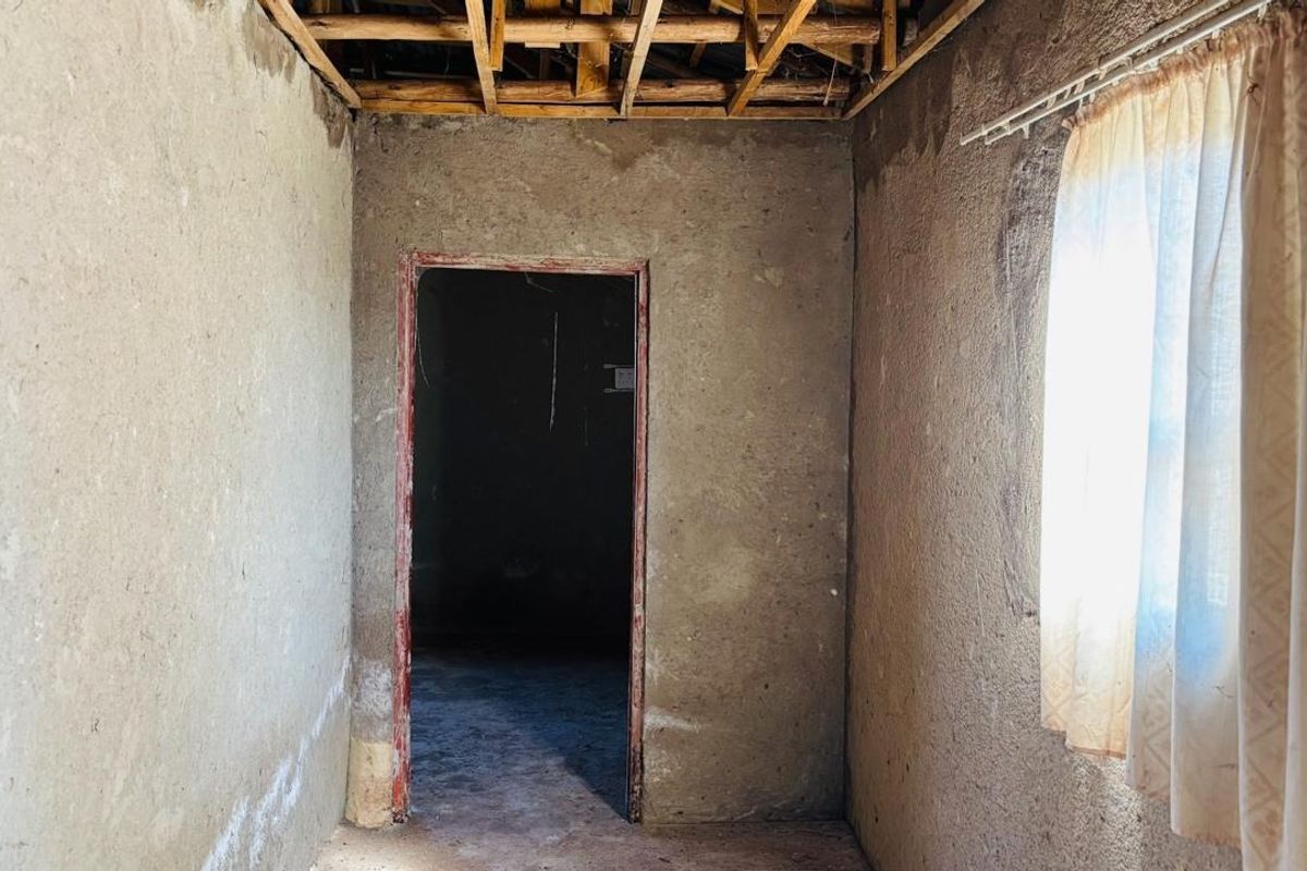 An unfinished bedroom interior featuring exposed timber ceiling joists and raw plastered walls, requiring significant renovation and finishing work.