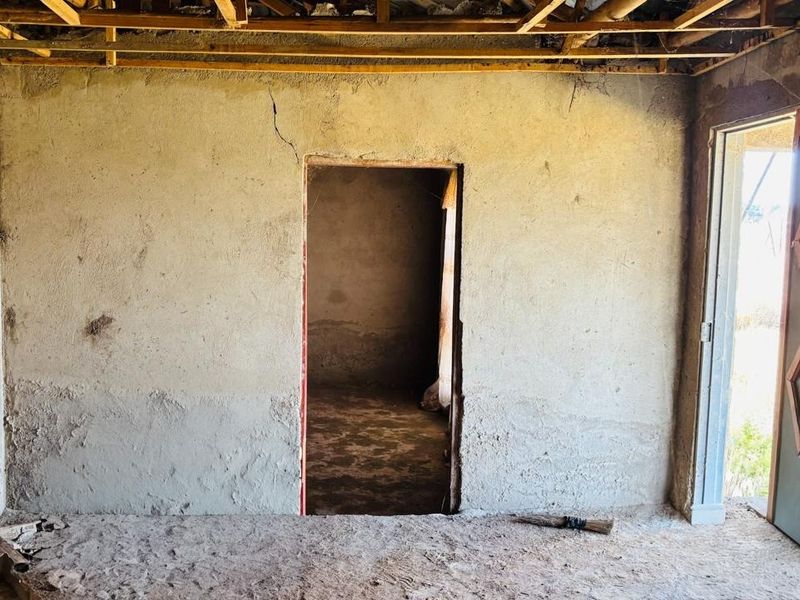 An unfinished interior space featuring exposed timber ceiling joists, raw plastered walls with visible cracks, and an installed external door.