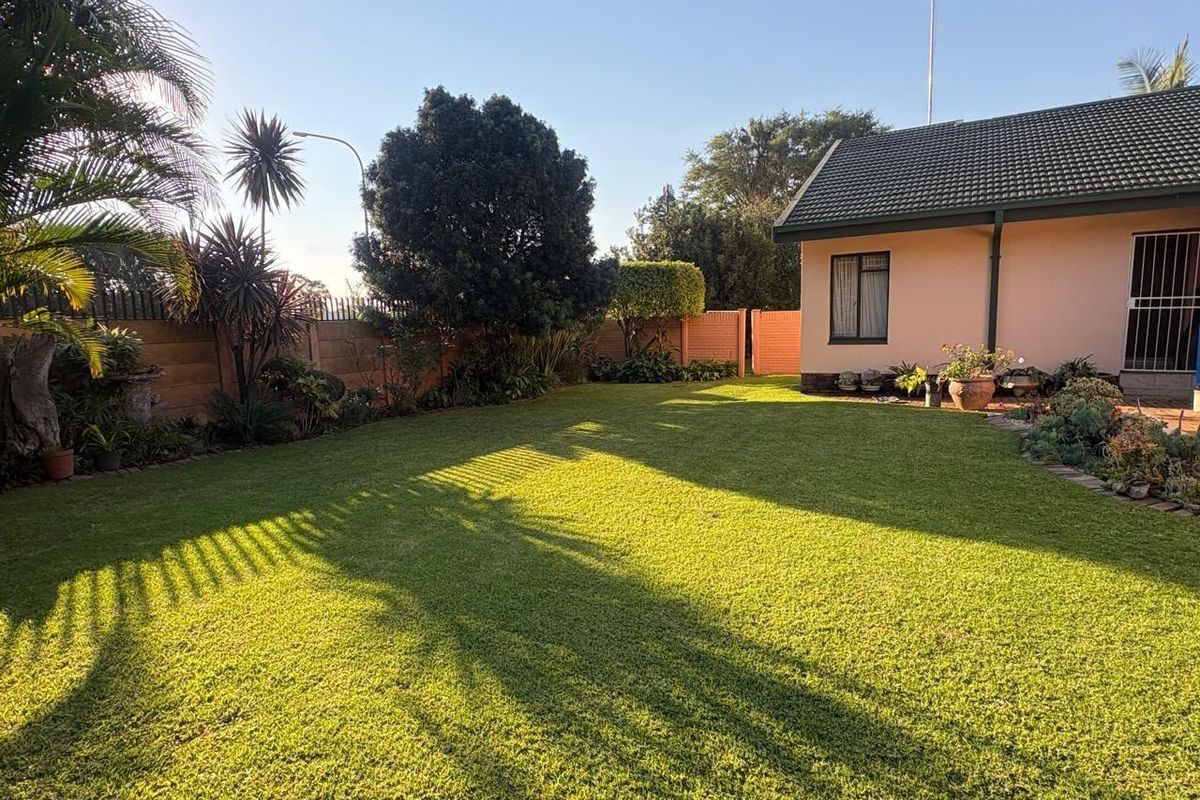 A well-maintained rear garden featuring a lush green lawn, enclosed by a secure precast concrete boundary wall and adjacent to the house exterior.